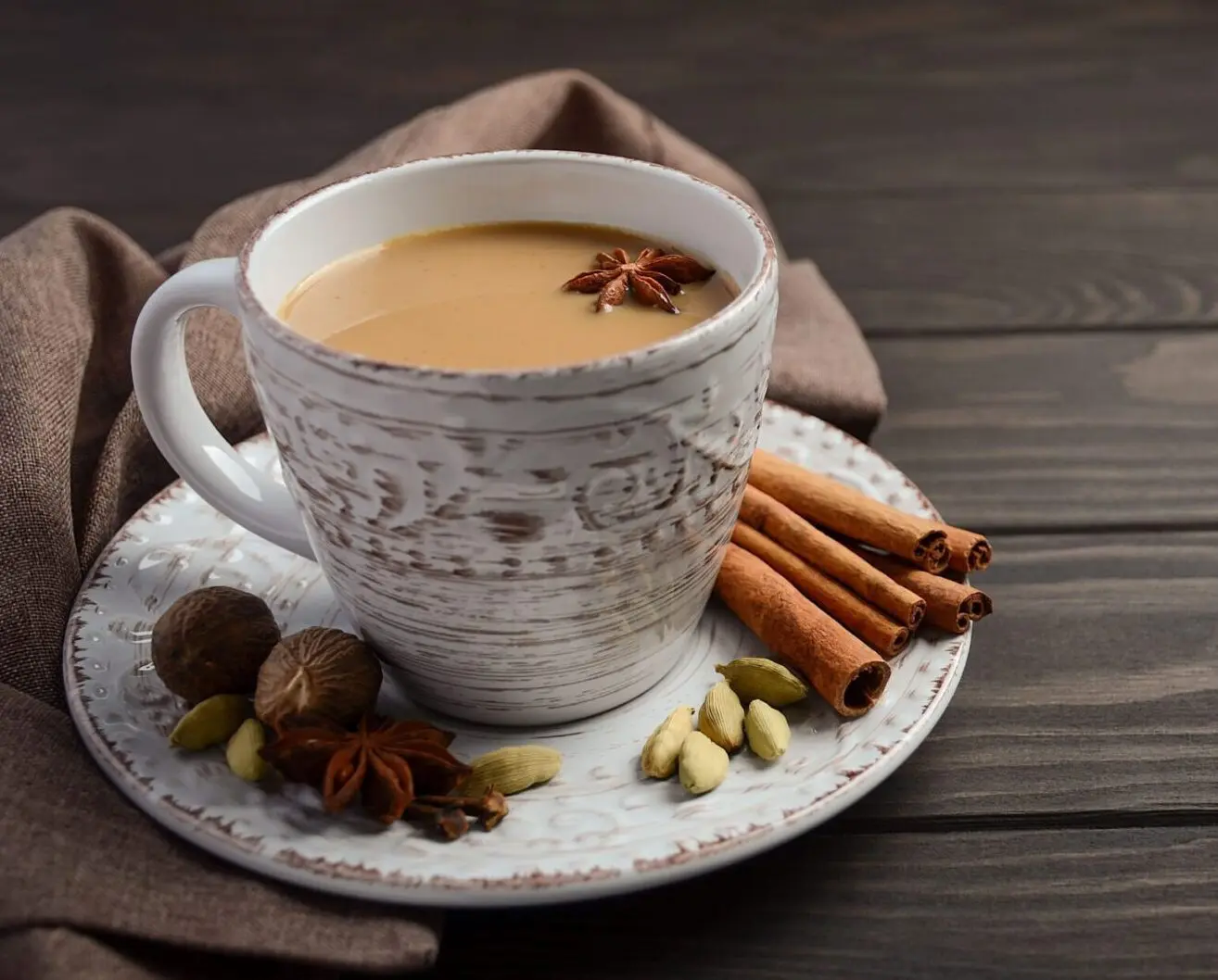 A cup of coffee with cinnamon sticks and nuts on the side.